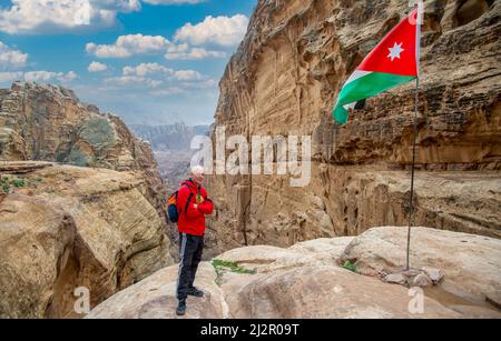 Ein Tourist posiert neben der jordanischen Flagge, die in Petra fliegt, mit schönen roten Bergen im Hintergrund und blauem Himmel 20. Februar 2020 Stockfoto