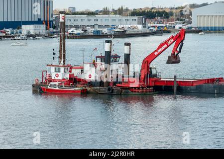 Bagger und Lastkahn, die einen Kanal in Portsmouth Harbour, Großbritannien, räumen Stockfoto