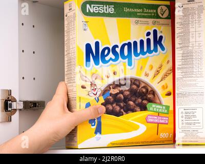 Tambov, Russische Föderation - 19. Februar 2022 Frau, die Nestle Chocolate Nesquik Müslibox aus einem Küchenschrank nimmt Stockfoto