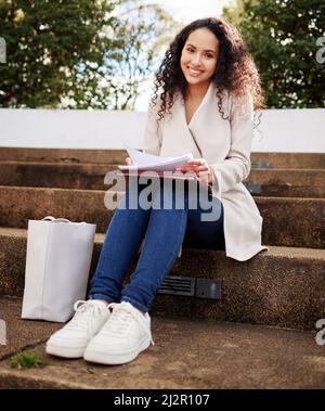 Ich hole mein Studium auf. Porträt einer attraktiven jungen Universitätsstudentin, die während ihrer Pause draußen auf dem Campus studiert. Stockfoto