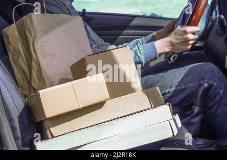 Kurier mit Paketen im Auto. Lieferung von Paketen, Waren, Pizza. Lieferer. Sichere Lieferung während der Quarantäne des Coronavirus. Stockfoto