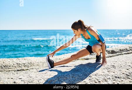 Auf ihre Fitnessziele hinzuarbeiten. Aufnahme einer jungen Frau, die sich vor ihrem Lauf dehnt. Stockfoto