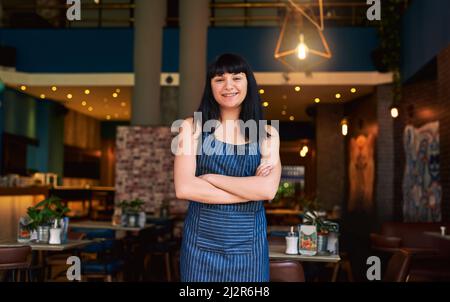 Selbstbewusst für die Betreuung der Kunden verantwortlich. Aufnahme einer Kellnerin, die am Eingang einer Bar steht. Stockfoto