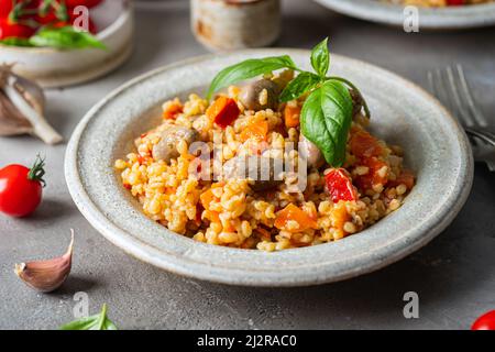 Bulgur mit Hühnerherzen und Gemüse. Leckeres gesundes Gericht auf grauem Hintergrund. Bulgur Pilaf Stockfoto