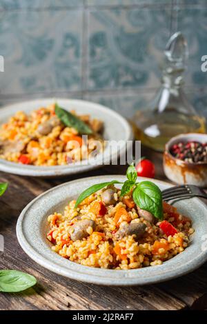 Bulgur mit Hühnerherzen und Gemüse. Köstliches gesundes Gericht auf dunklem Hintergrund. Bulgur Pilaf Stockfoto