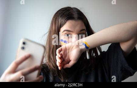 Ein ukrainisches Mädchen mit einer gemalten Flagge der Ukraine auf ihrem Gesicht macht ein Selfie. Stockfoto