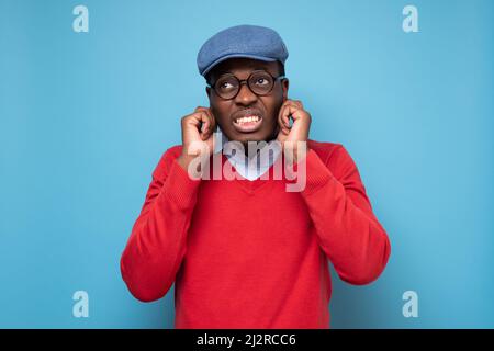 Junger afrikanischer Mann verstopft Ohren mit Fingern, um laute Geräusche zu vermeiden. Stockfoto