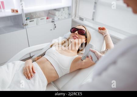 Freudige Frau, die im Schönheitssalon eine Laserepilation erhält Stockfoto