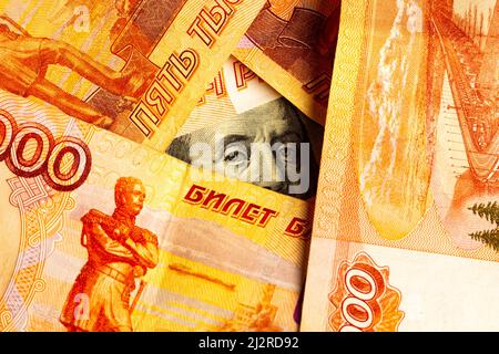 Russische Rubel sind um US-Dollar angeordnet. Das Konzept des Wechselkurses, der Sanktionen, des Rückgangs des Rubels, der Prävalenz der Währungen. Stockfoto