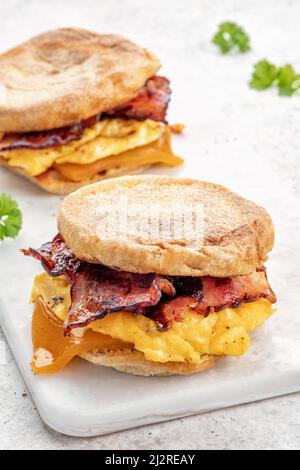 Englisches Muffin, Ei, Schinken und Käse-Frühstückssandwich auf einem Schneidebrett Stockfoto