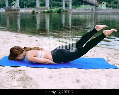 Junge fit Frau in Sportbekleidung in verschiedenen Yoga-Asanas draußen am Strand am Fluss. Yoga- und Sportkonzept Stockfoto