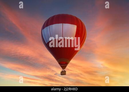 Roter Heißluftballon, der bei Sonnenuntergang oder Sonnenaufgang am Himmel fliegt Stockfoto