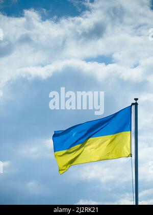 Die Flagge der Ukraine weht in Solidarität mit den Menschen in der Ukraine gegen einen wolkenblauen Himmel. Stockfoto