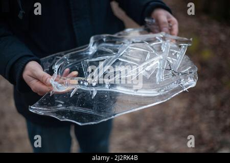 Eis in den Händen. Kalter Frühlingshintergrund. Ein Fragment gefrorenen Wassers. Der Kerl hält ein Glasstück Wasser in den Händen. Stockfoto