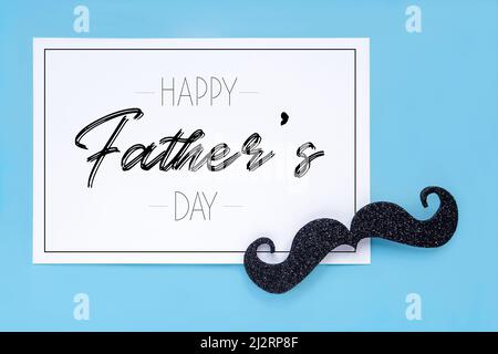 Nahaufnahme eines Schnurrbartens und einer Karte mit dem Ausdruck glücklicher Vatertag auf blauem Hintergrund. Kopieren Sie den Platz für Beschriftungen. Stockfoto