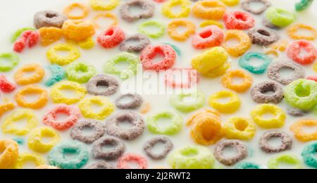 Schnelles Vollkornfrühstück. Mehrfarbige Fruchtringe in der Milch. Nahaufnahme. Viele Objekte. Fastfood, Kinder, Schulessen. Vitamine, gesundes Leben Stockfoto