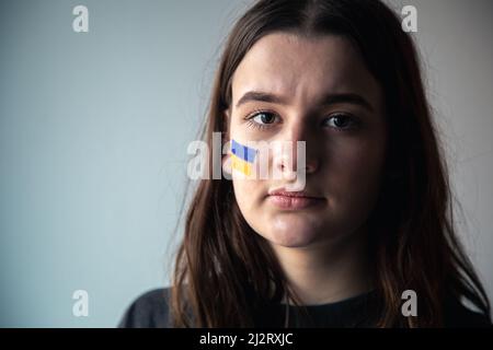 Ein ukrainisches Mädchen mit einer gemalten Flagge der Ukraine auf ihrem Gesicht. Stockfoto