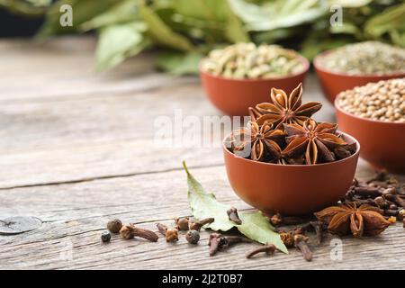 Schale mit Anissternen. Schalen mit aromatischen Gewürzen - Koriander, Kardamom-Schoten auf dem Hintergrund. Handschuhe, Lorbeerblätter. Zutaten für gesundes Kochen. Ayurveda Stockfoto