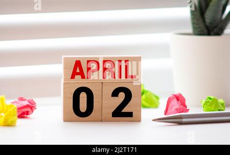 Weißer Vintage Holzblock Kalender präsentieren Datum 02 und Monat April auf blauem Holztisch über abstrakten grünen Bokeh Hintergrund mit Kopieplatz. Stockfoto
