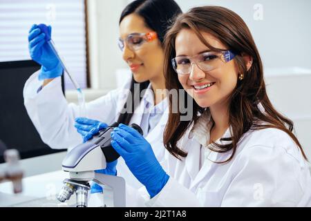 Zwei schöne junge Wissenschaftlerinnen, die im Labor mit Reagenzgläsern und Mikroskop arbeiten, um in der pharmazeutischen Industrie zu forschen Stockfoto