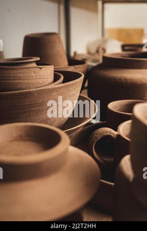 Regale mit Schüsseln, Tellern, Gläsern, Teekannen usw. aus Ton in natürlicher Rohfarbe bis zum endgültigen Gemälde. Kunsthandwerk aus Lehm. Vertikale Ausrichtung. Stockfoto