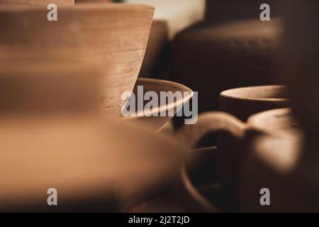 Regale mit Schüsseln, Tellern, Gläsern, Teekannen usw. aus Ton in natürlicher Rohfarbe bis zum endgültigen Gemälde. Kunsthandwerk aus Lehm. Nahaufnahme. Stockfoto