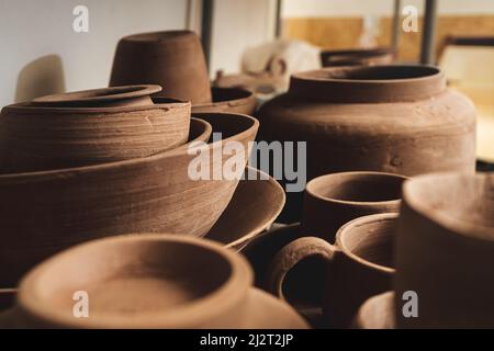 Regale mit Schüsseln, Tellern, Gläsern, Teekannen usw. aus Ton in natürlicher Rohfarbe bis zum endgültigen Gemälde. Kunsthandwerk aus Lehm. Stockfoto