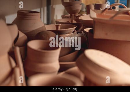 Regale mit Schüsseln, Tellern, Gläsern, Teekannen usw. aus Ton in natürlicher Rohfarbe bis zum endgültigen Gemälde. Kunsthandwerk aus Lehm. Stockfoto