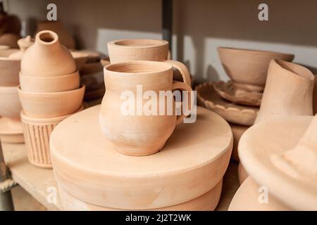 Regale mit Schüsseln, Tellern, Gläsern, Teekannen usw. aus Ton in natürlicher Rohfarbe bis zum endgültigen Gemälde. Kunsthandwerk aus Lehm. Stockfoto