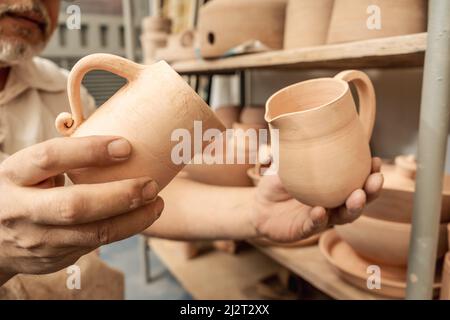 Töpferhandwerker überprüft Tongefäße und organisiert die Regale bis zum endgültigen Gemälde. Handgemachtes Kunsthandwerk aus Lehm. Stockfoto