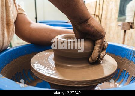 Die erfahrenen Hände eines Töpfers, der Ton auf einem Töpferrad arbeitet. Der Ton nimmt die Form an, die der Töpfer ihm mit dem Terrakotta-Ton des Tones gibt. Stockfoto