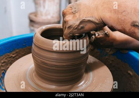 Die erfahrenen Hände eines Töpfers, der Ton auf einem Töpferrad arbeitet. Der Ton nimmt die Form an, die der Töpfer ihm mit dem Terrakotta-Ton des Tones gibt. Stockfoto