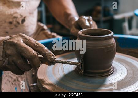 Die erfahrenen Hände eines Töpfers, der Ton auf einem Töpferrad arbeitet. Der Ton nimmt die Form an, die der Töpfer ihm mit dem Terrakotta-Ton des Tones gibt. Stockfoto