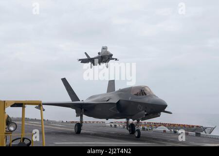 220401-N-XN177-1012 PAZIFISCHER OZEAN (1. April 2022) – ein F-35B Lightning II-Flugzeug, das an das Marine Fighter Attack Squadron (VMFA) 211 angeschlossen ist, landet auf dem Flugdeck, während sich ein weiteres auf den Start an Bord des amphibischen Angriffsschiffs USS Tripoli (LHA 7) am 1. April vorbereitet. VMFA-211 wird an Bord von Tripolis als Teil der U.S. Marine Corps "Lightning Carrier Concept Demonstration. Die Lightning Carrier Concept Demonstration zeigt, dass Tripolis und andere amphibische Angriffsschiffe in der Lage sind, als dedizierte stationäre Trägerplattformen zu arbeiten, die in der Lage sind, den Kurzstart/die vertikale Landung der fünften Generation (ST Stockfoto