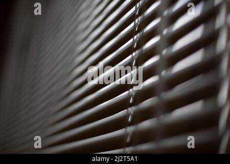 Jalousien am Fenster. Weiße Jalousien bedecken das Fenster vor der Sonne. Details zur Innenausstattung. Diagonal aufnehmen. Stockfoto