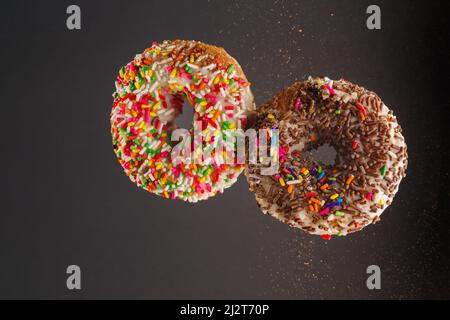 Nahaufnahme. Zwei bunte Donuts im gefrorenen Flug auf grauem Hintergrund. Süßes Essen, Kalorien, Geburtstag, Frühstück, romantisches Date, Valentinstag. Shop, Stockfoto