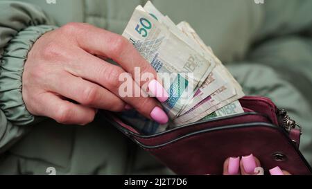 Nahaufnahme der weiblichen Hände nehmen Zloty-Banknoten aus einem fliederfarbenen Geldbeutel, polnischer Währung, heraus. Das Konzept des Währungswechsels in einem anderen Land. Tourismus und Stockfoto