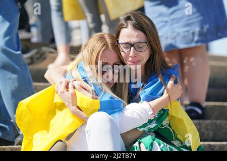 St. Louis, Usa. 03. April 2022. Eingewickelt in eine ukrainische Flagge, weinen Frauen, als sie sich umarmen, auf den Stufen des Gateway Arch in St. Louis am Sonntag, dem 3. April 2022. Die ukrainische Gemeinschaft versammelte sich am Bogen mit gespendeten Stofftieren, die die Hunderte von Kindern darstellen, die während der aktuellen russischen Invasion getötet wurden. Die Versammlung umfasste Worte der Ermutigung, Gebete und ukrainische Musik. Foto von Bill Greenblatt/UPI Credit: UPI/Alamy Live News Stockfoto