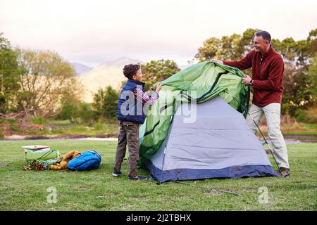 Das Camp ist fast fertig. Aufnahme eines Vaters und eines Sohnes, der während des Campens zusammen ein Zelt aufgeschlagen hat. Stockfoto