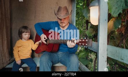 Papa Cowboy spielt für sein kleines Kind eine akustische Gitarre. Altes Retro-Dekor Stockfoto