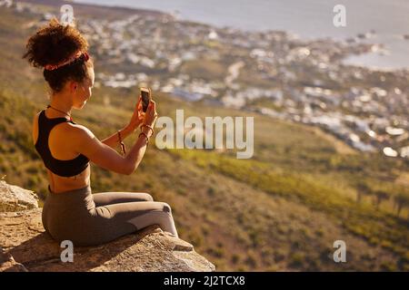 Mal sehen, wie viele „Gefällt mir“-Angaben dieses hier erhalten werden. Aufnahme einer Frau, die mit ihrem Handy Fotos machte, während sie auf einer Bergklippe saß. Stockfoto