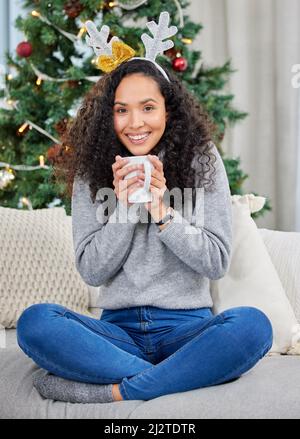 Zu Hause gemütlich machen. Aufnahme einer jungen Frau, die während der Weihnachtszeit zu Hause Kaffee trinkt. Stockfoto