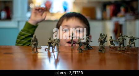 Der kleine Junge jubelt über Spielzeugsoldaten, während er mit einem vorgetäuschten Kampf spielt Stockfoto