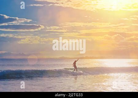 Silhouette eines Surfers, der an einem heißen Sommertag auf Bali eine kleine Welle reitet Stockfoto