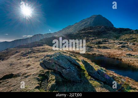 Szene mit Hintergrundbeleuchtung, Snowdonia National Park, sonniges Wetter Mitte März, Blick vom Watkin Path auf den Mount Snowdon Summit, in die direkte Sonneneinstrahlung Stockfoto