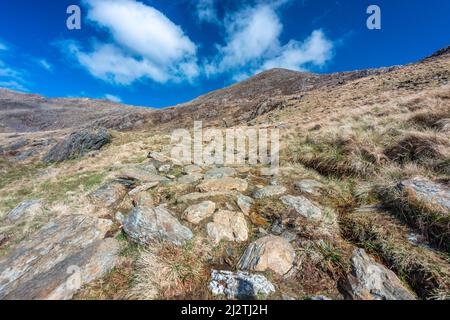 Eine lange und steile Route hinauf zum Gipfel des Mount Snowdon, an einem sonnigen Tag im März mit felsigen schmalen Wegen, lockeren Geröll und schöner Aussicht auf Snowdonia Stockfoto