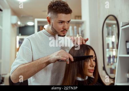 Professioneller männlicher Friseur, der im Schönheitssalon der Frau Frisur macht Stockfoto