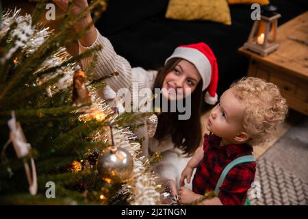 Eine Teenager-Schwester zeigt ihrem jüngeren Bruder die Ornamente auf dem Weihnachtsbaum. Stockfoto