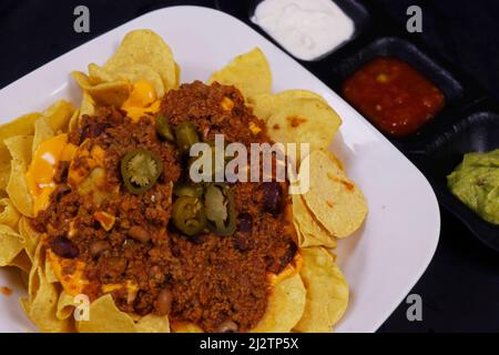 Traditionelle mexikanische Snacks, Mais-Tortilla-Chips und Avocado-Guacamole, Chili con Carne, Salsa und saure Creme. Bekannt als Nachos Stockfoto