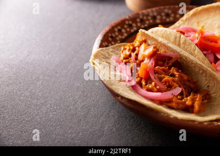Tacos de Cochinita Pibil. Typisch mexikanischer Eintopf aus Yucatan, hergestellt aus Schweinefleisch, mariniert mit Achiote und in der Regel mit Bohnen und roten Zwiebeln begleitet Stockfoto